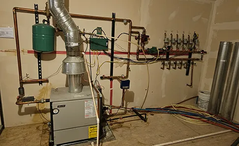 A boiler room before the work, with an older boiler and exposed piping