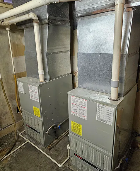 Two old furnaces with worn ductwork in a basement, before replacement